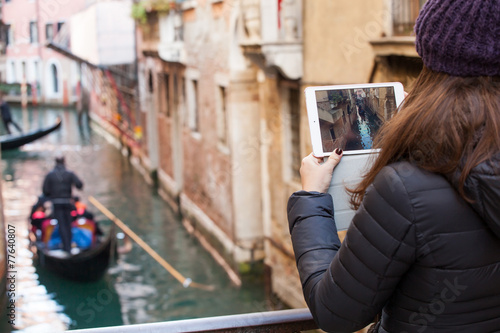 Young girl using a tablet to take pictures of gondolas of Venice