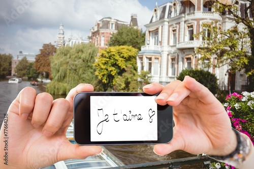 Composite image of hand holding smartphone showing je taime photo