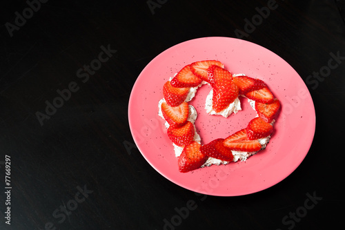 heart shaped strawberry in a pink plate on black background