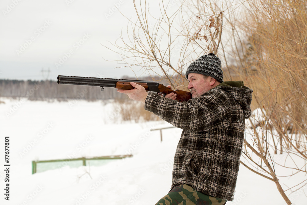 Fototapeta premium A hunter shooting a rifle in winter snowy landscape