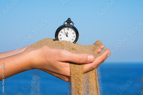 pocket clock in hands and sand flowing