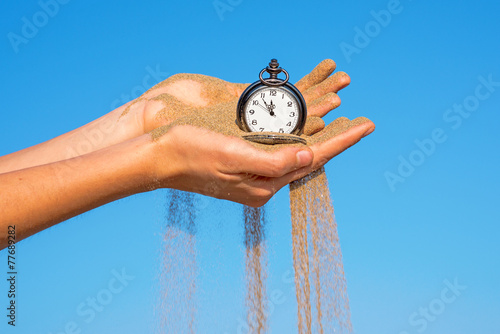 pocket clock in hands and sand flowing