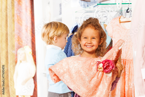 Laughing girl holds dress, boy behind her in shop