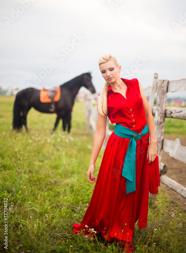 Beautiful young woman in red dress with a horse outdoor