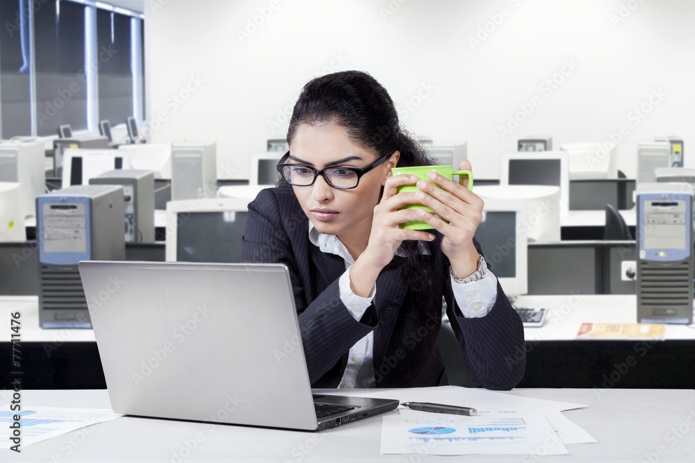 Female manager with laptop holding coffee