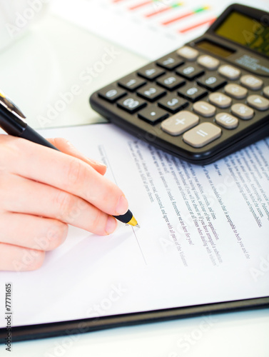 Woman at office desk signing a contract with shallow focus on si