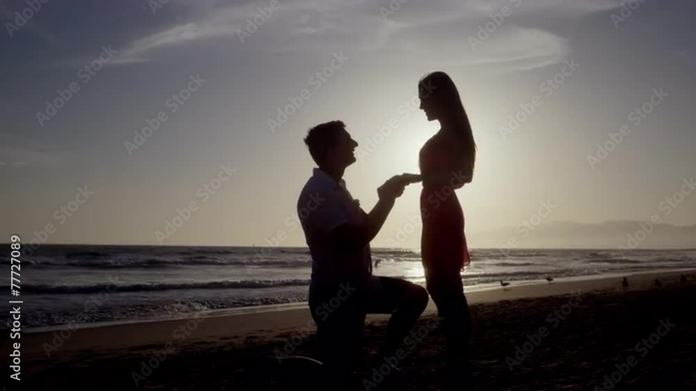 man proposing marriage to woman on one knee - will you marry me - silhouette on beach by ocean - romantic proposal putting ring on finger to be married - 4K slow motion man proposing marriage to woman on one knee - will you marry me - silhouette on beach by ocean - romantic proposal putting ring on finger to be married - 4K slow motion