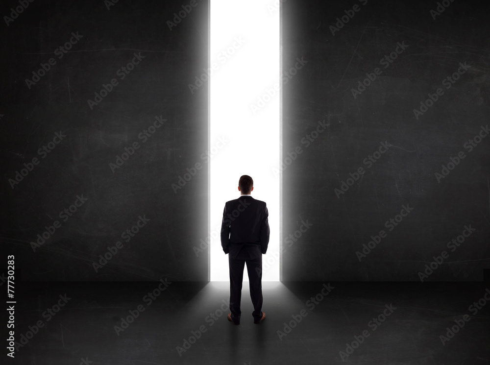 Business person looking at wall with light tunnel opening Business person looking at wall with light tunnel opening