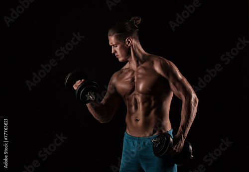 Closeup of a muscular young man lifting weights on dark backgrou © romanolebedev