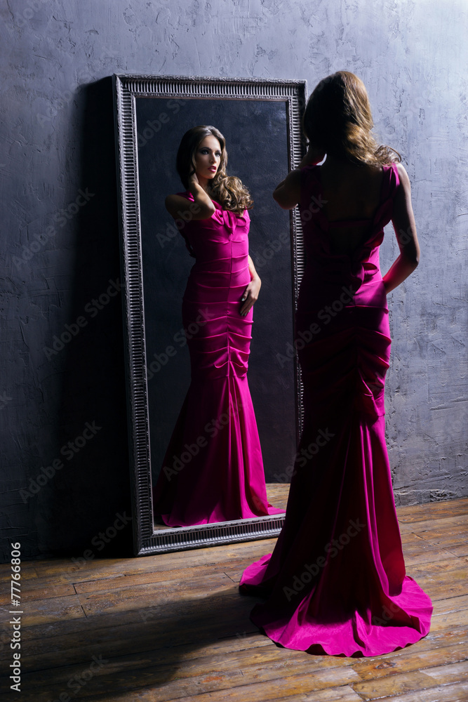 Young actress in a long dress in front of the mirror