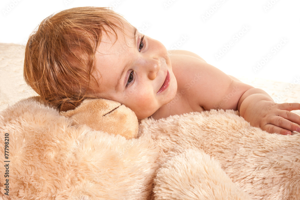 Charming little boy lies on a beige soft faux fur bear.
