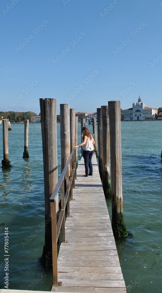 Woman walking down a wooden footbridge with mooring posts for gondolas on a canal in venice