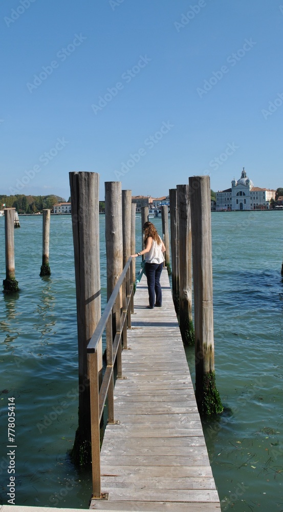 Woman walking down a wooden footbridge with mooring posts for gondolas on a canal in venice Woman walking down a wooden footbridge with mooring posts for gondolas on a canal in venice