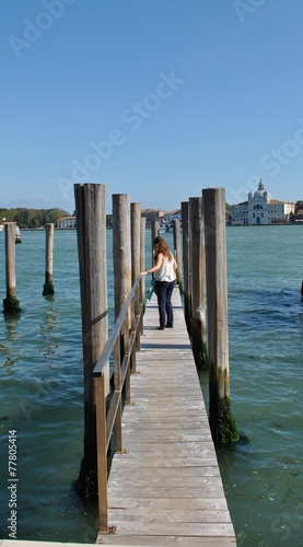 Woman walking down a wooden footbridge with mooring posts for gondolas on a canal in venice