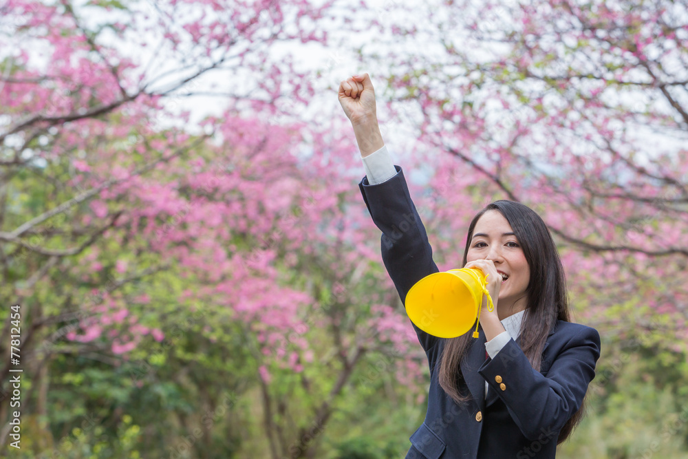 桜をバックにメガホンで応援をする女子学生