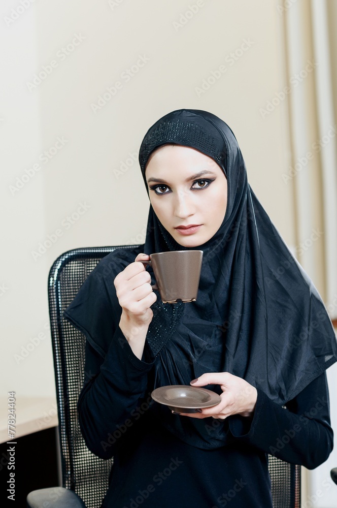 Muslim woman drinking coffee while sitting in an office chair Muslim woman drinking coffee while sitting in an office chair