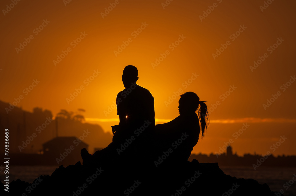 Silhouette of man and women against sunset over a harbor