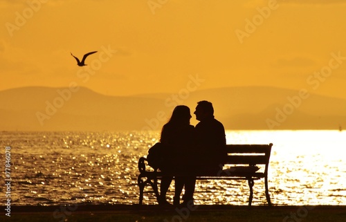 Young couple sitting on a bench under sunset