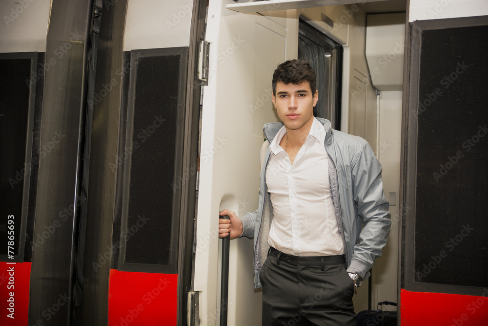 Handsome young man on train, standing in open door threshold