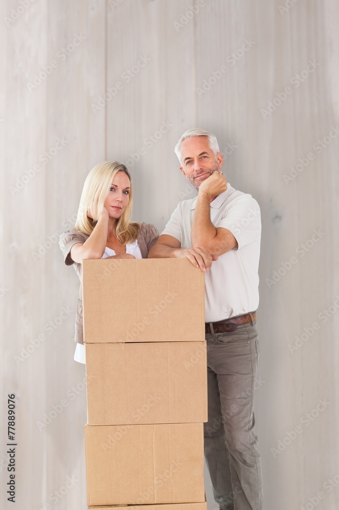 Composite image of happy couple leaning on pile of moving boxes Composite image of happy couple leaning on pile of moving boxes