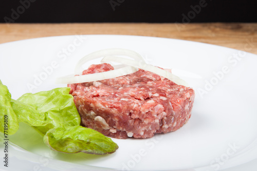 Raw cutlet, onion and salad on a white plate