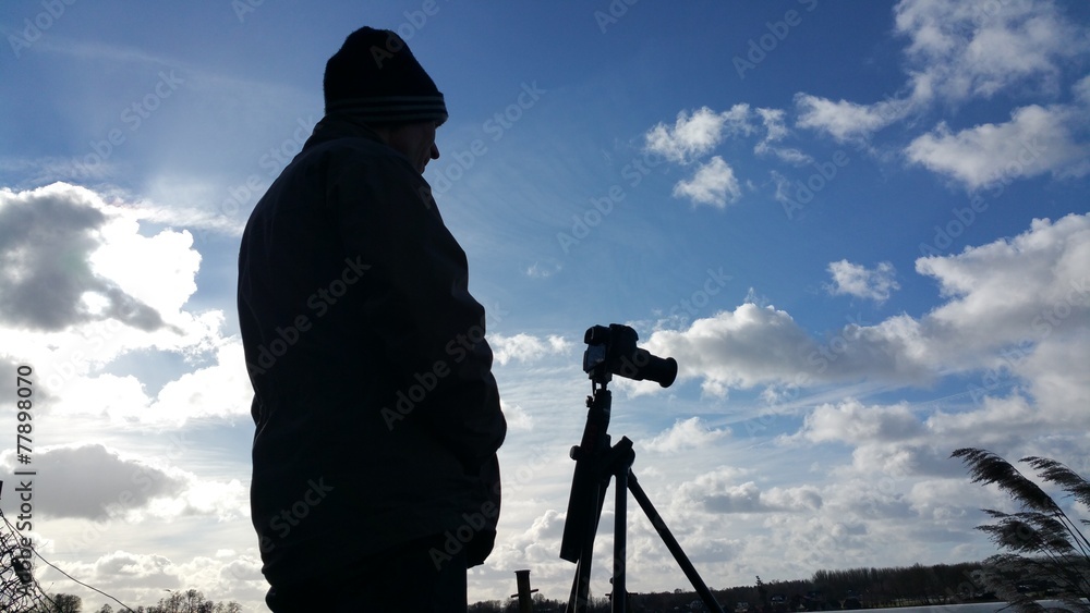 Silhouette eines Fotografen mit Mütze gegen einen bewölkten Himmel im Winter aus niedriger Perspektive