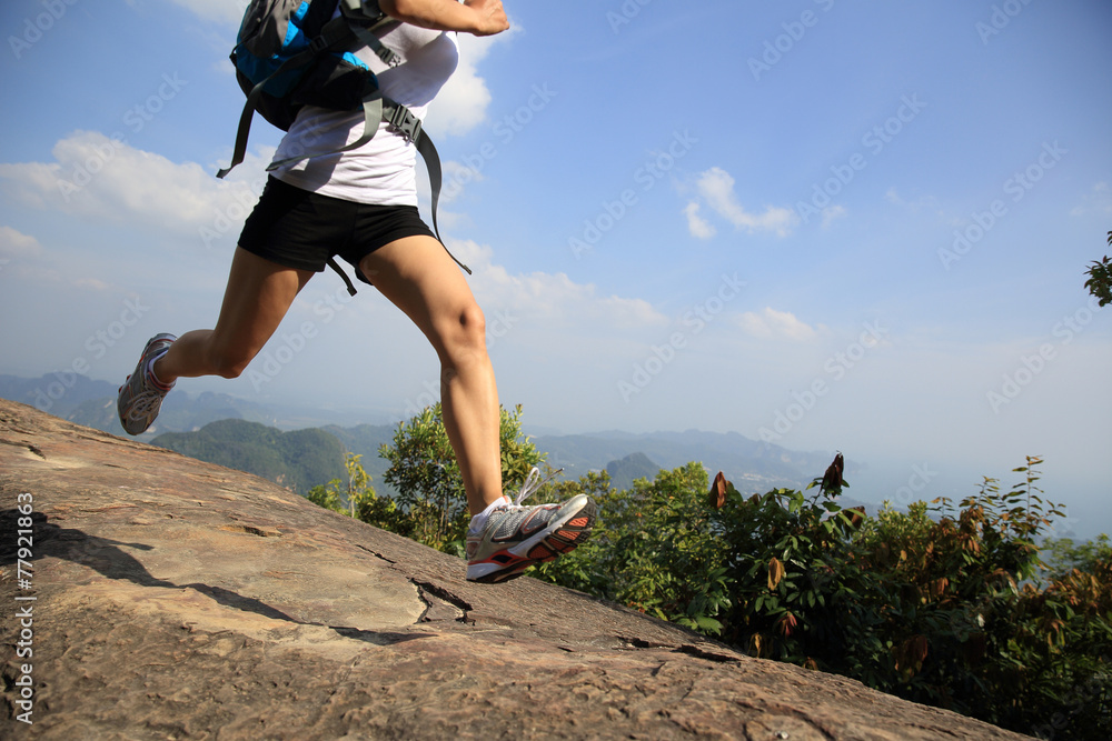 woman hiker running at on mountain peak rock