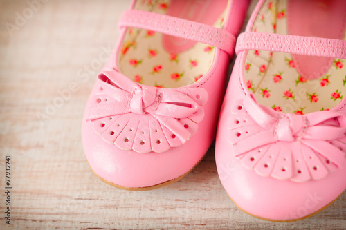 Detail of a pink girl shoes over wooden deck floor.