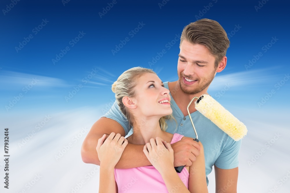 Composite image of young couple hugging and holding paint roller Composite image of young couple hugging and holding paint roller