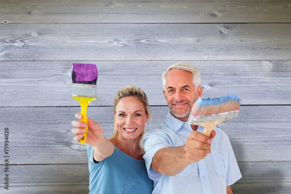 Happy couple holding paintbrushes smiling at camera Happy couple holding paintbrushes smiling at camera