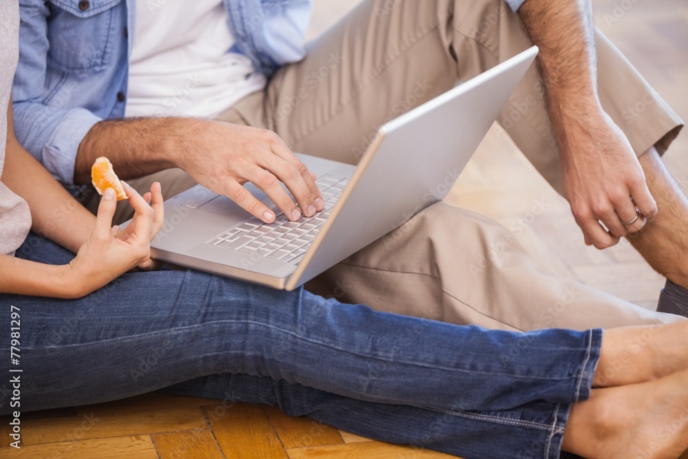 Mid section of couple sitting on floor using laptop