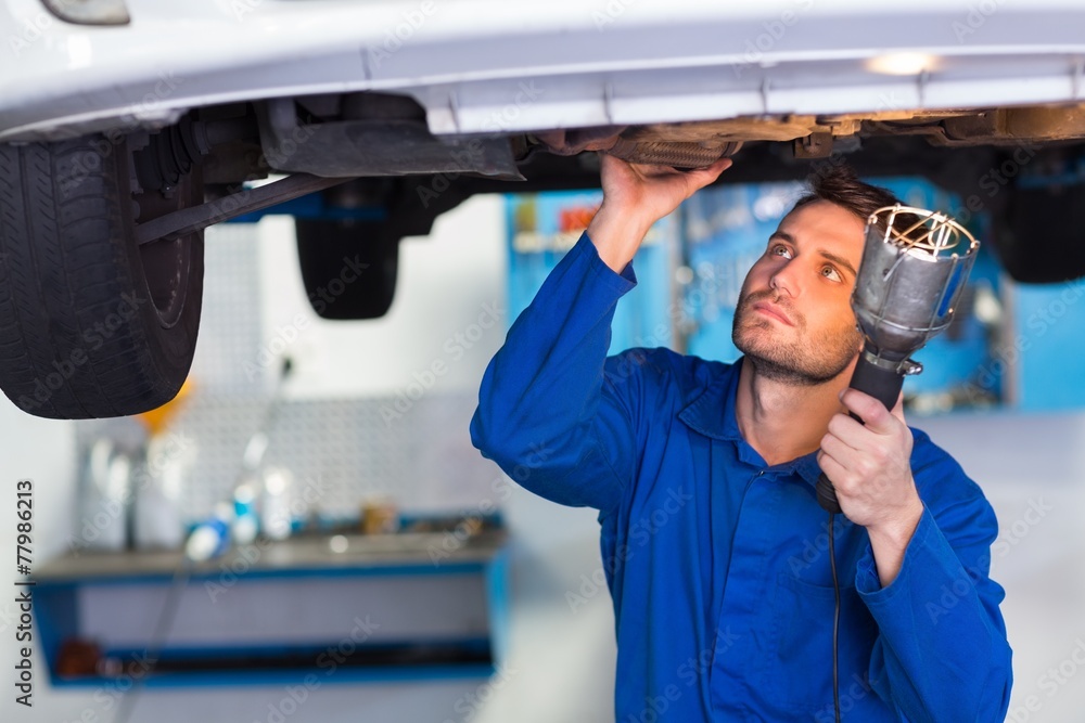 Mechanic examining under the car with torch Mechanic examining under the car with torch