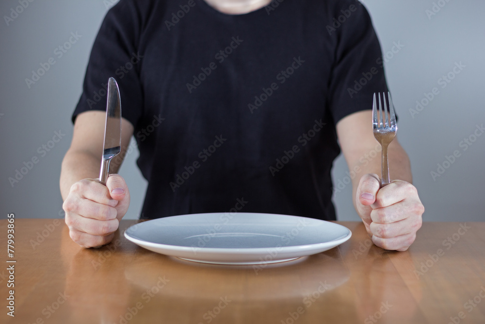 © tuomaslehtinen - Man sitting at a table waiting for food, holding fork and knife