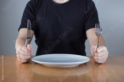 Fototapeta Man sitting at a table waiting for food, holding fork and knife