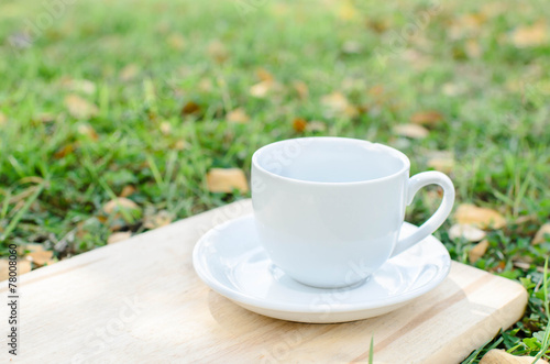 Blank coffee cup on wooden board with grass and natural light.