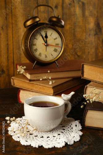 Cup of tea with books and clock on wooden background