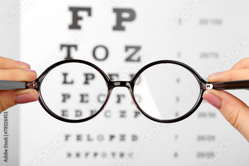 Glasses in hands on eye chart background, close-up