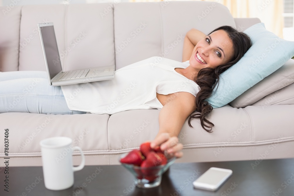 Pretty brunette lying on couch using laptop Pretty brunette lying on couch using laptop