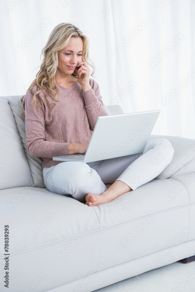 Smiling blonde sitting on couch using laptop Smiling blonde sitting on couch using laptop