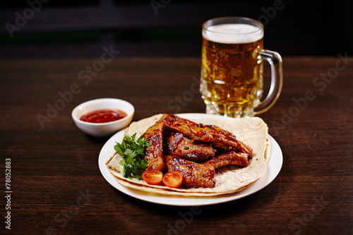 Plate with roasted pork ribs on wooden table