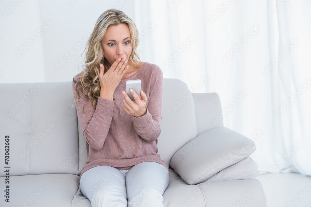 Surprised blonde sitting on couch reading message Surprised blonde sitting on couch reading message
