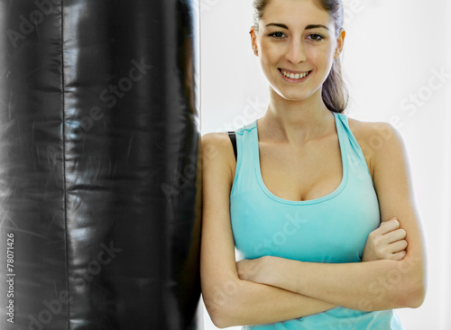 Young smiling brunette is standing next to a punching bag © Francesco83