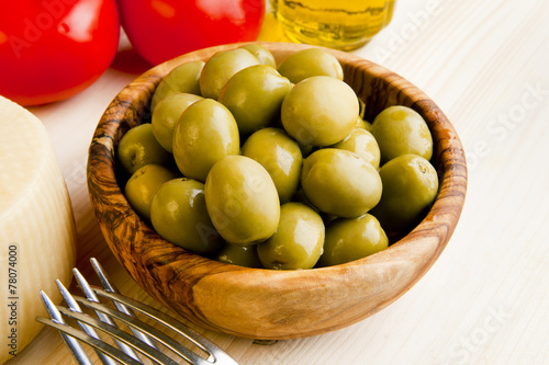 green olives in wooden bowl & tomato, parmesan cheese