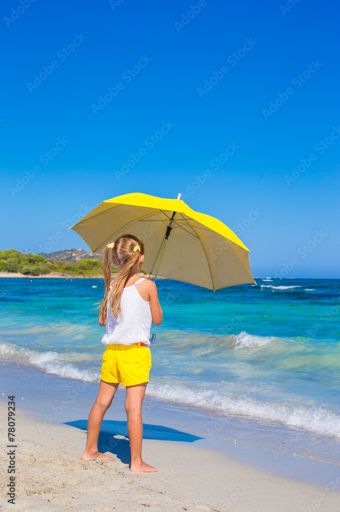 Little adorable girl with big yellow umbrella on tropical beach