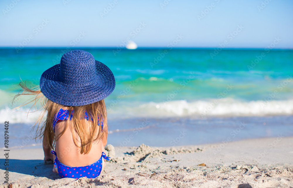 Adorable little girl in big blue straw hat at white beach