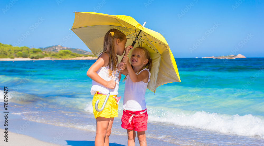 Little girls with big yellow umbrella during tropical beach