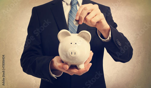 Young man depositing money in piggy bank