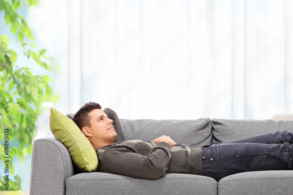 Fototapeta premium Relaxed young man lying on a sofa at home