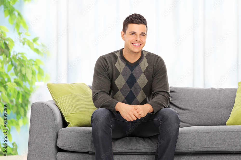 Young man posing seated on a sofa at home