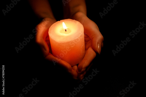 Candle in female hands on black background